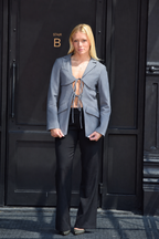 A blonde woman stands in front of a black door wearing a light gray cropped blazer over a beige tie-front top and black wide-leg pants.